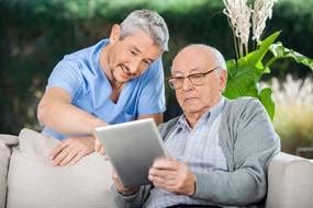 Male caretaker assisting senior man in using digital tablet at nursing home porch